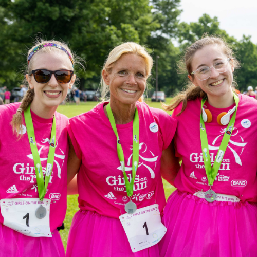 Three smiling alumni wearing pink Girls on the Run t-shirts and finisher medals.